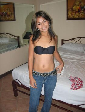 Pinay bargirl takes off a shirt to pose in a strapless bra and jeans on a bed