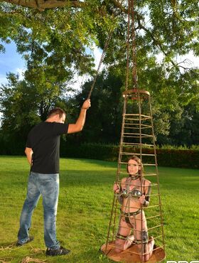 Inked submissive babe Lauren poses in an outdoor cage while chained