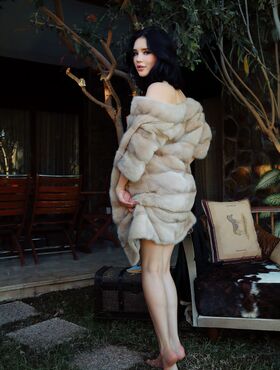 Beautiful dark haired teen removes a fur coat to model naked on a patio