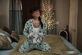 Tattooed babe in glasses Jessie Lee flashes her big fake tits on a bed